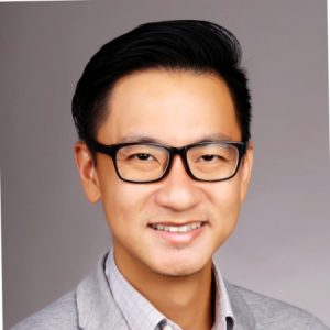 Face Adrian Tan person with glasses and suit on grey background