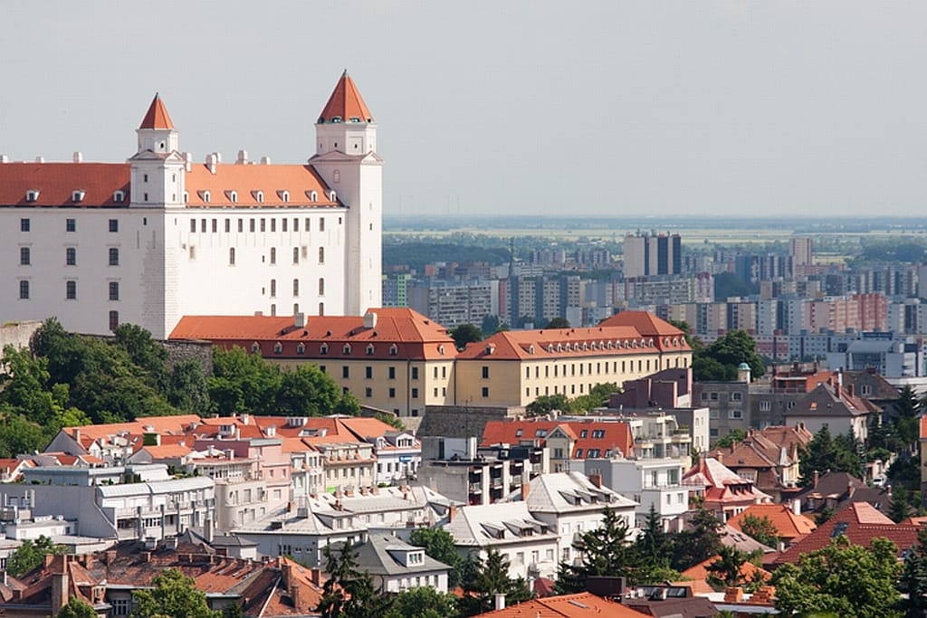 Cityscape of Bratislava Slovakia featuring Bratislava Castle the old town and the modern city beyond with a lot of buildings old and new green fields in the background and a grey sky