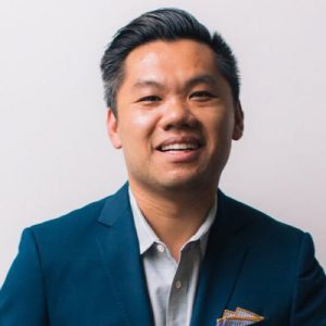 Andrew Chen with black hair navy blue suit and blue shirt on a grayish background