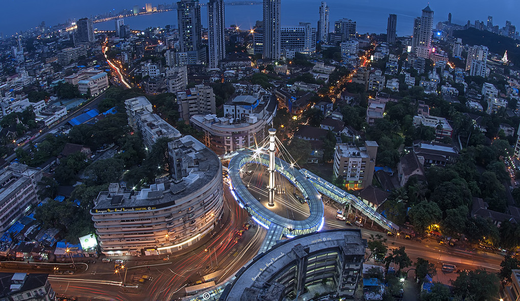 view of Mumbai India at night featuring many building green trees and the sea in the background