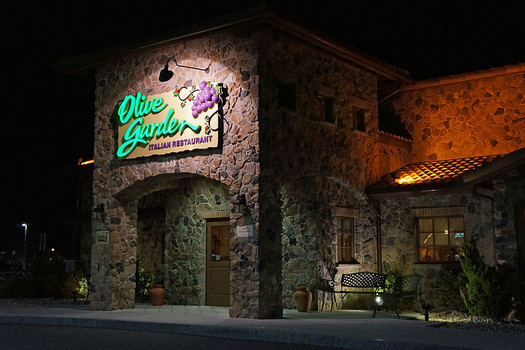 exterior of a stone-walled restaurant with a green and purple neon sign above the door at night