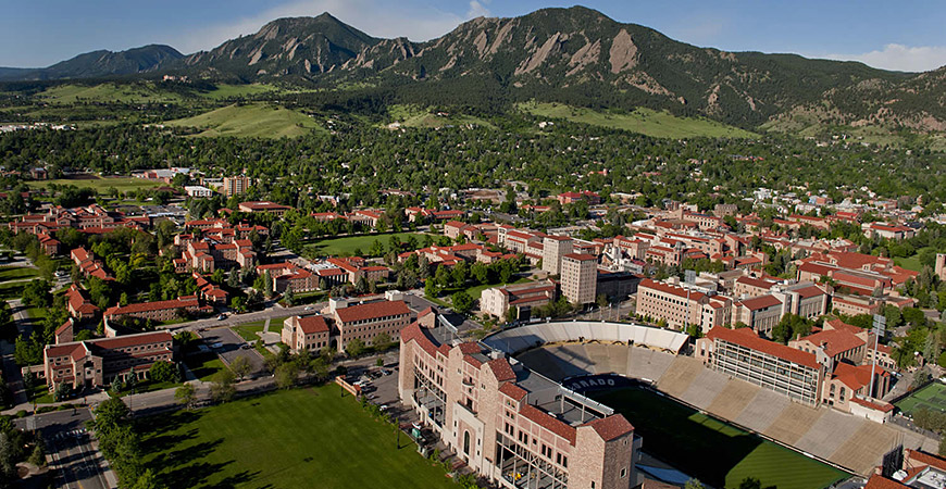 University of Colorado campus in Boulder featuring Boulder stadium university buildings student accommodation with a backdrop of green mountains and blue sky