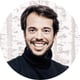 man smiling, brown hair, beard, scarf, black tshirt, white background with grey lines