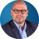 man, light blue shirt, dark blue suite, glasses, bold, blue background