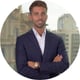man, standing holding hands, watch, smiling, white shirt, dark blue suit, brown hair, short beard