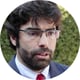 man, talking, white shirt, red tie, dark black suit, curly brown hair, glasses, beard