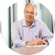man sitting and smiling, light blue shirt, bold, hodling pen, paper on the table