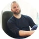 man, sitting and holding his knee, black seat, black tshirt, beard, short brown hair