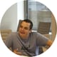 man, talking and explaining something, expressing with his right hand, grey tshirt, brown hair,office space, window behind him