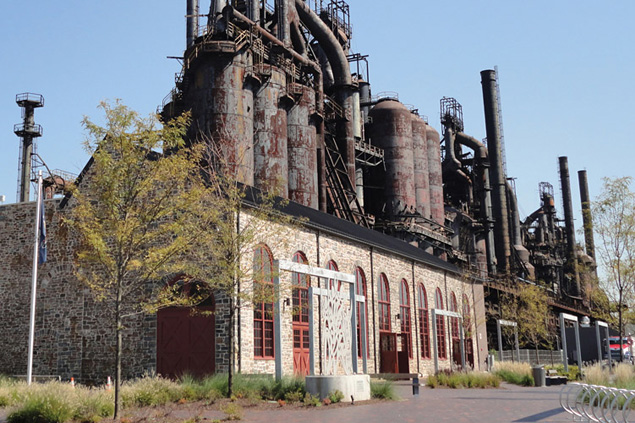 disused stell mill stands in front of a blue sky with greenery and trees in the foreground