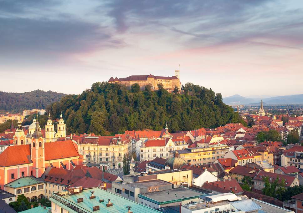 ljubljana slovenia old buildings orange roofs castle on the hill with green trees mountains sky clouds