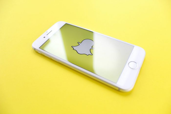 an white iphone displaying the snapchat logo on a yellow background
