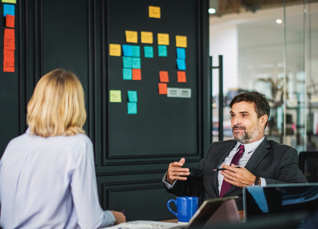 Adult are talking in an office where post-its taped on the wall