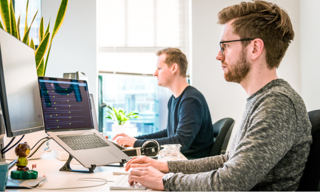 Two men working in an office, sitting in front of computer screens.