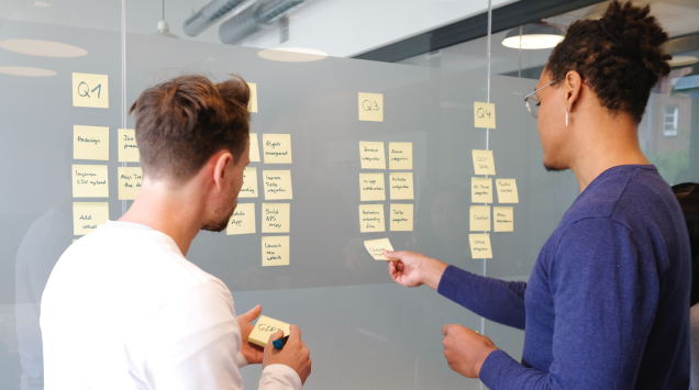 A man and a woman putting post-it notes on a board